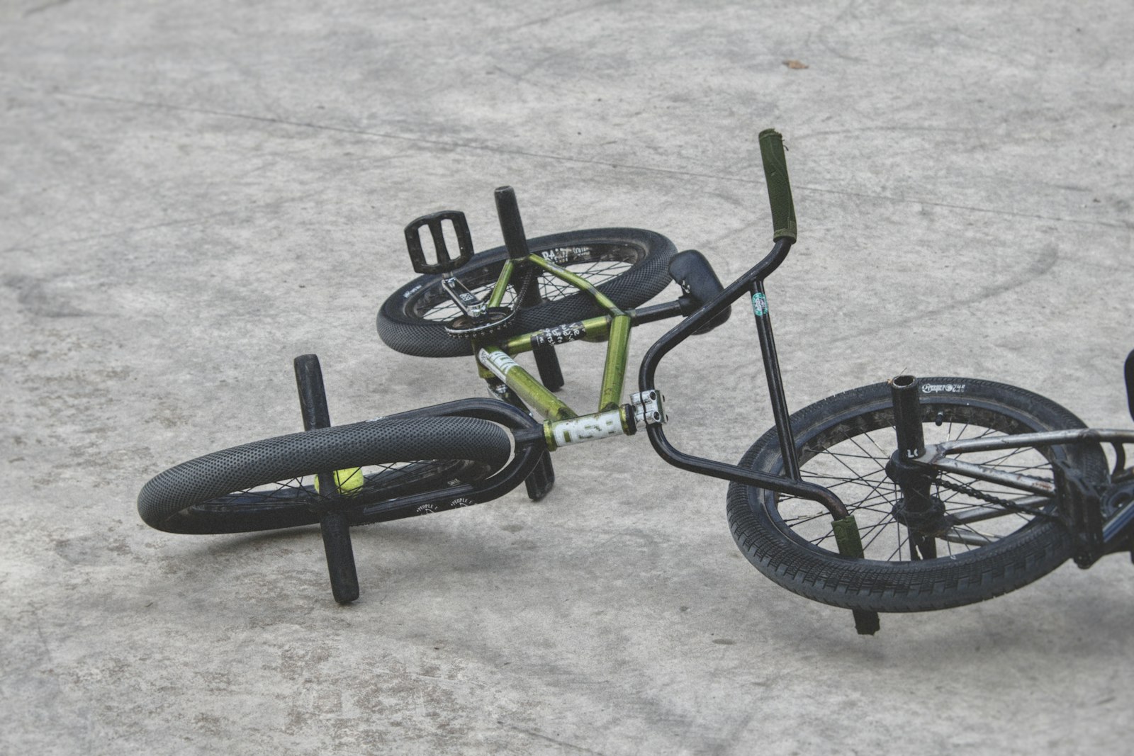 Vélo BMX vert et noir posé au sol sur le béton d'un skatepark