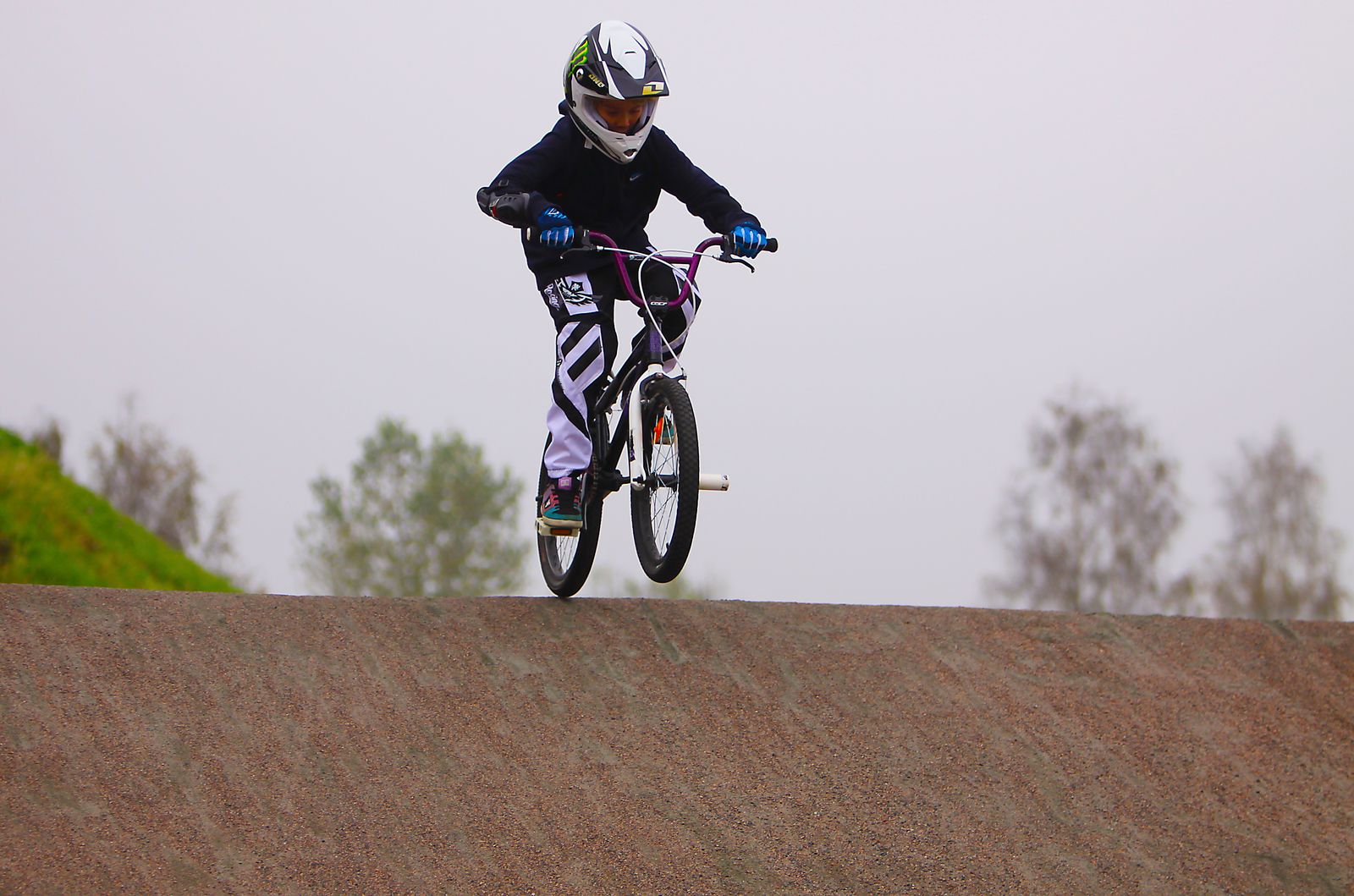 Pilote de BMX Race dévalant une pente sur une piste en terre