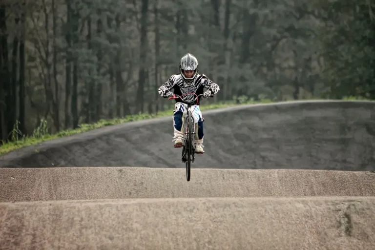 Pilote de BMX Race en casque intégral sautant une bosse sur une piste en terre