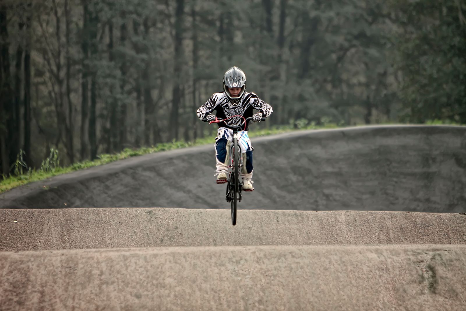 Pilote de BMX Race en casque intégral sautant une bosse sur une piste en terre