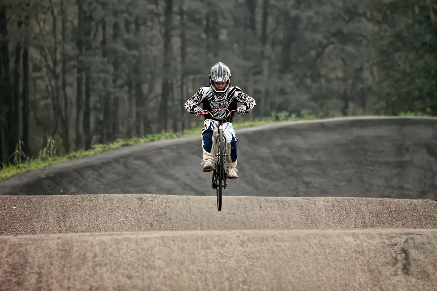Pilote de BMX Race en casque intégral sautant une bosse sur une piste en terre
