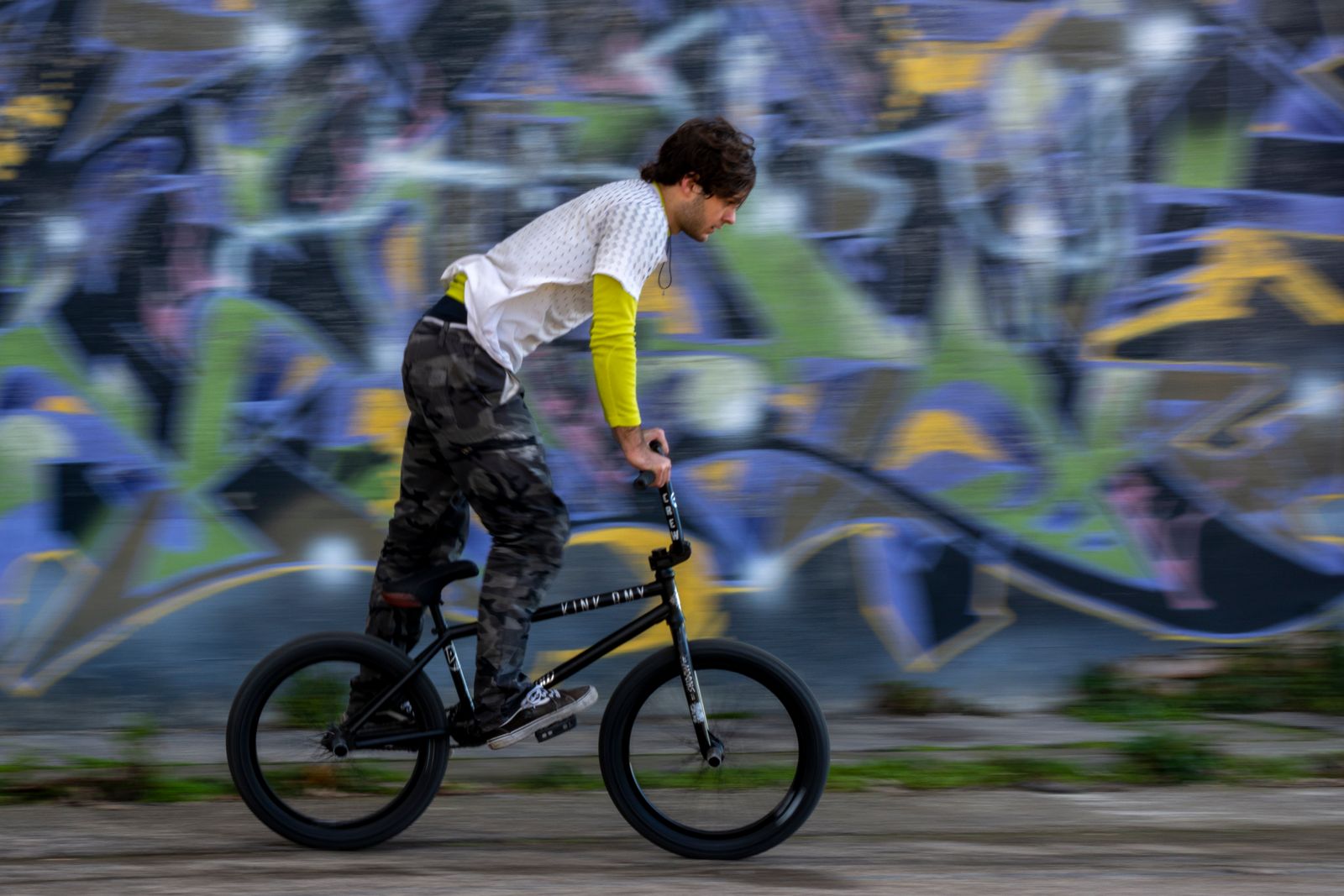 Rider de BMX en pleine figure devant un mur de graffitis en ville