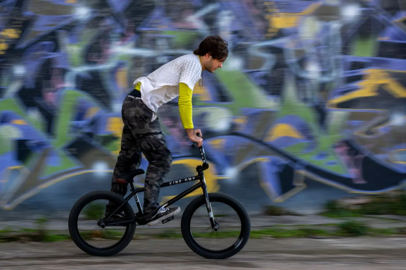 Rider de BMX en pleine figure devant un mur de graffitis en ville