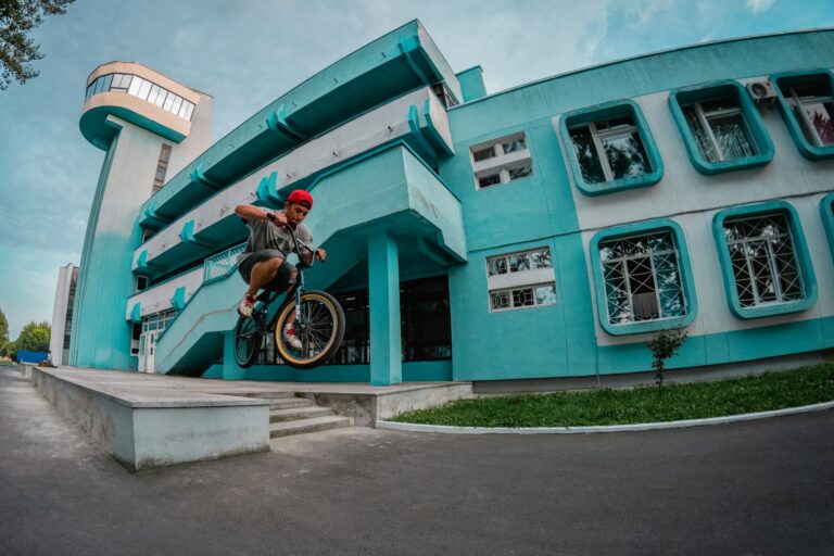 Rider de BMX en plein saut devant un bâtiment turquoise, les deux roues décollées