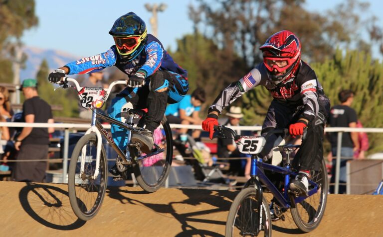 Deux pilotes de BMX Race en casque intégral au coude-à-coude sur une piste