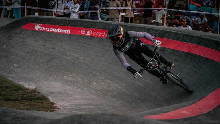 Rider en casque intégral penché dans un virage relevé de pumptrack en enrobé lors d'une compétition