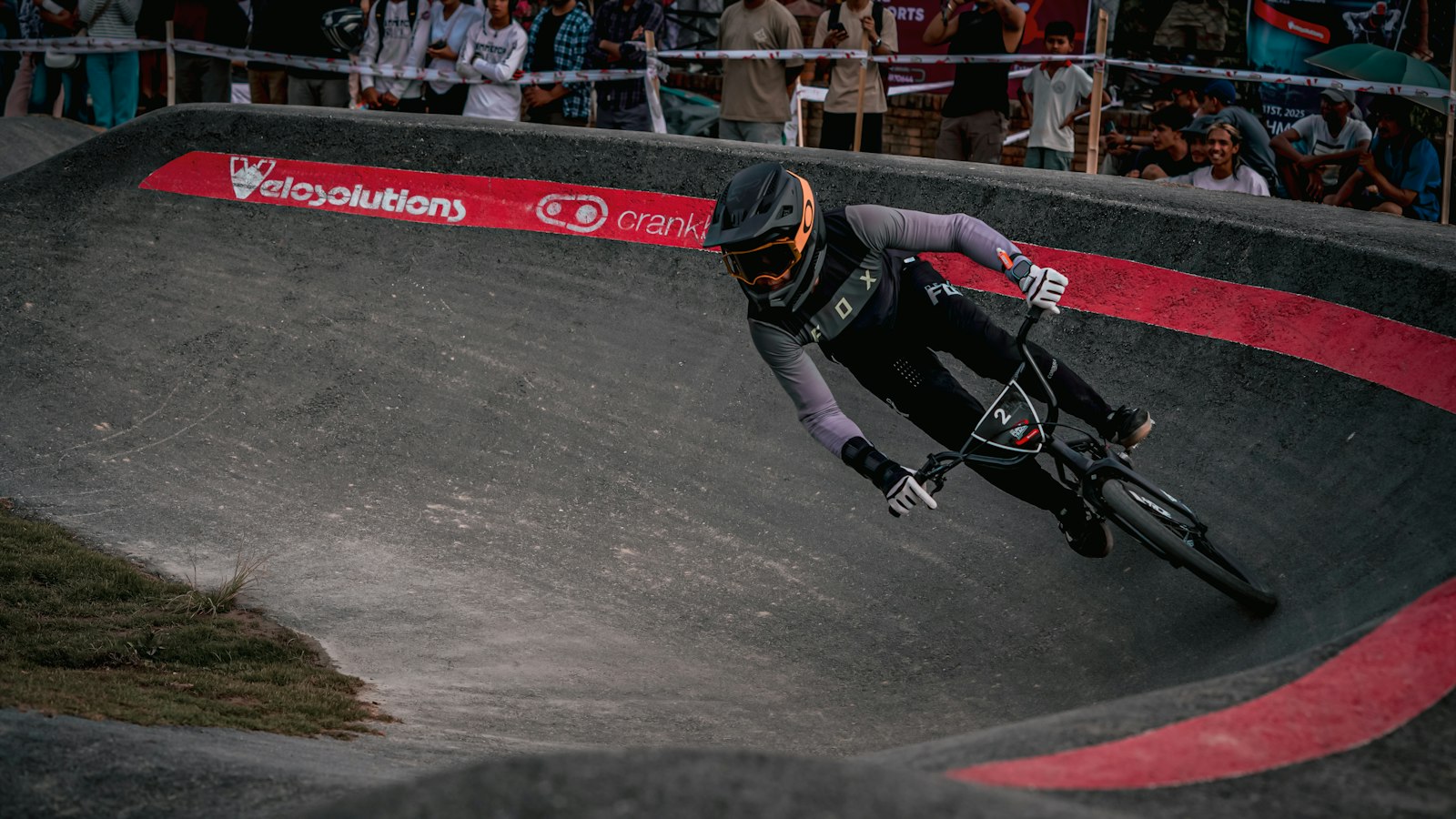 Rider en casque intégral penché dans un virage relevé de pumptrack en enrobé lors d'une compétition